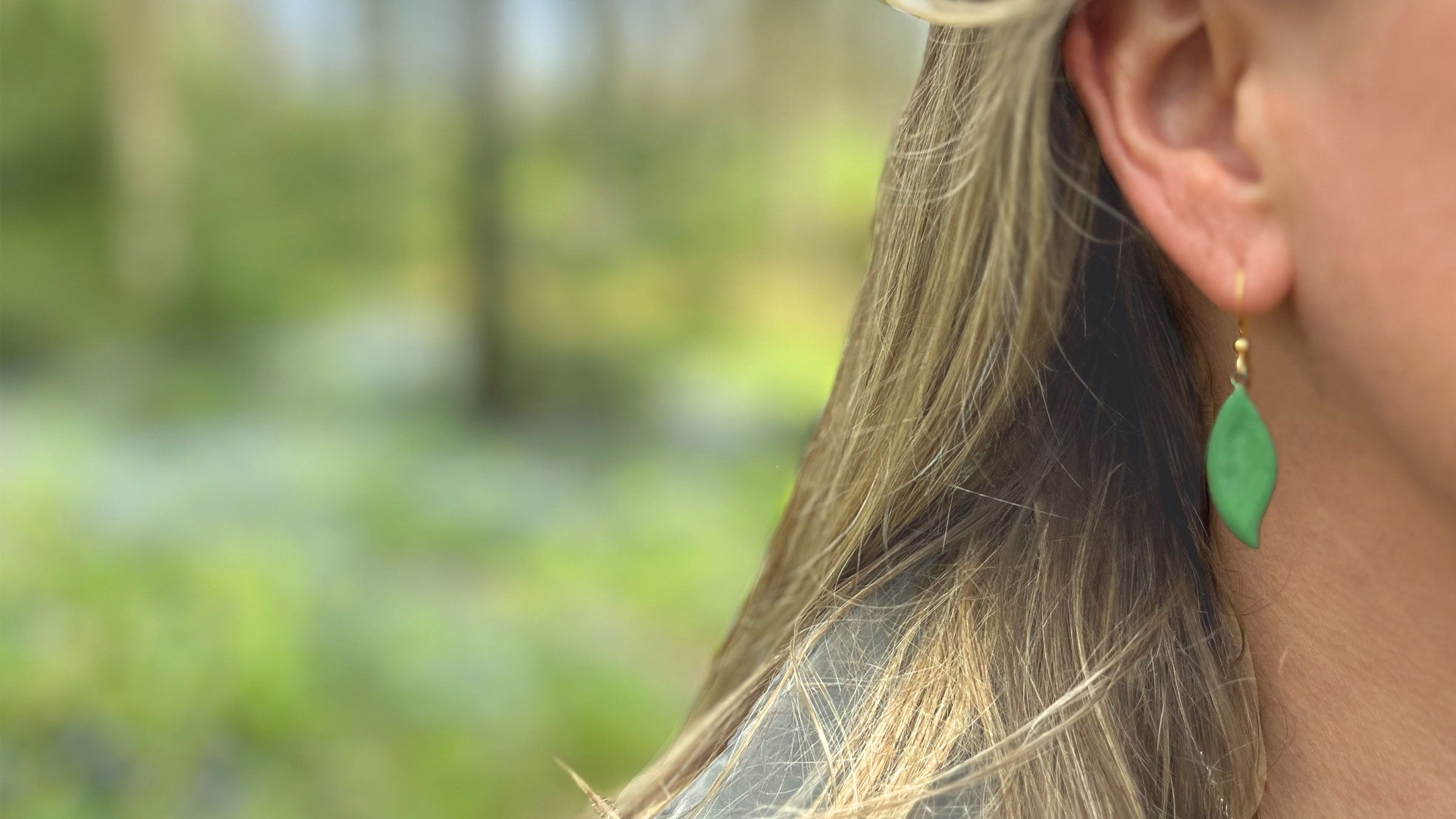 Close-up of a person wearing green leaf-shaped earrings with a blurred natural background