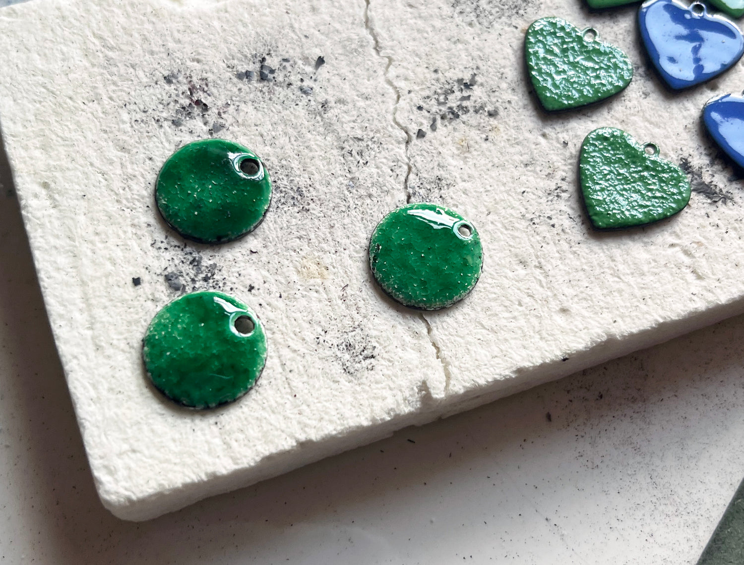 Green heart-shaped and domed enamel earring pieces on a textured white surface