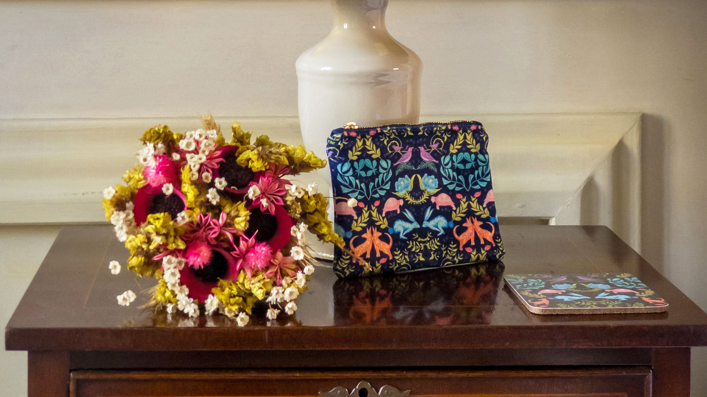 Colorful floral arrangement and patterned pouch on a wooden surface with a neutral background